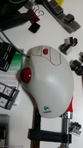 Trackman Marble+ -pallohiiri, jossa punainen peukalopallo ja keskisormen alla rulla. Kolme hiiren nappia etusormelle, keskisormelle ja nimettömälle.